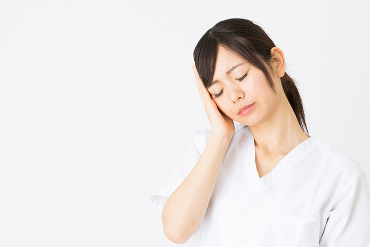 頭痛のため首を傾げ手を当てる女性