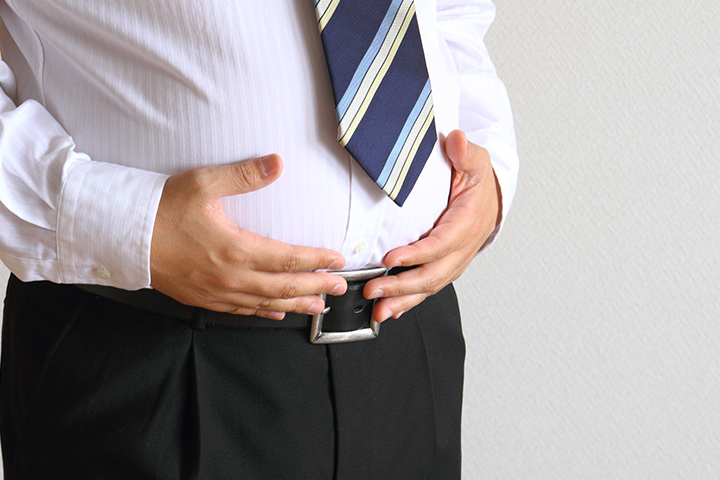 腹部を両手でおさえる肥満気味の男性
